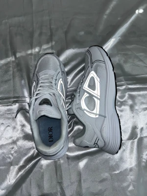 Grå  sneakers med reflekterande detaljer - Snygga grå sneakers från  med reflekterande detaljer på sidorna och meshpaneler för extra andningsförmåga. Skorna har en chunky sula och klassisk snörning. Perfekta för dig som vill sticka ut med exklusiv streetstyle.