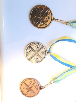Guld, silver och bronsmedaljer - Dessa föremål är samlarobjekt i form av tre simmedaljer med blå-gula band, dessa har jag kammat hem helt själv under mina tävlingar. Håll gärna utkik på min profil, har fler och kommer säkert lägga upp mer i framtiden.. Design: Motivet visar de fyra simsätten (fjärilsim, ryggsim, bröstsim och frisim), vilket gör den till ett klassiskt samlarobjekt för simidrottsentusiaster. De finns i guld, silver och brons, vilket tyder på första, andra och tredje pris. * Det är inte rent guld, silver eller bro