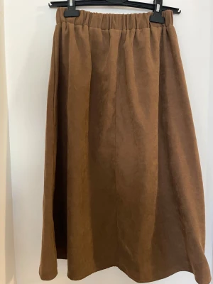 Brun kjol med resårmidja - Säljer en brun kjol i mjuk manchester liknande material  med resår i midjan. Kjolen har en rak och enkel design med lätt utställd form och når ungefär till vaden. 