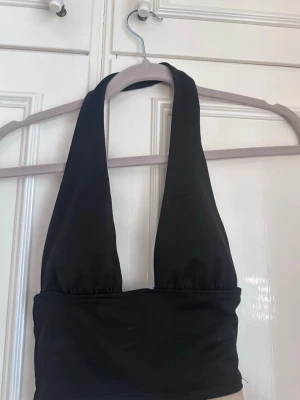 Svart halterneck topp - Snygg svart halterneck topp med breda band som knyts i nacken. Toppen är croppad och har en tight passform, perfekt till jeans eller en kjol. Tillverkad i mjukt och stretchigt material för en bekväm känsla.