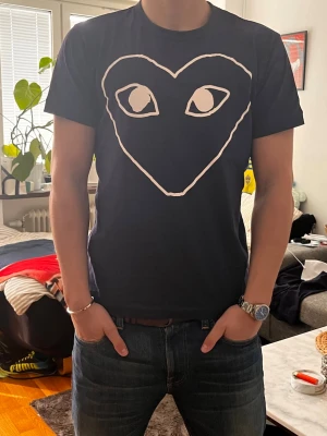 Marinblå  Comme des Garçons t-shirt  - Marinblå t-shirt från Comme des Garçons med det ikoniska hjärtmotivet med ögon på bröstet. T-shirten har rund halsringning och korta ärmar. Perfekt för dig som vill sticka ut med en unik design. Är 184cm lång. Skriv vid frågor eller funderingar!😊