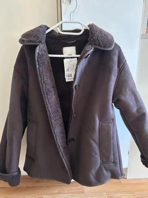 Mörkbrun teddyjacka med krage - Mysig mörkbrun teddyjacka med knäppning framtill och bred krage.  Perfekt för kyliga dagar och ger en trendig look. Den är helt ny och oanvänd. Det är storlek xxs men passar som en xs/s då jag själv är S i vanliga fall. 