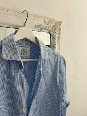 Rutig skjorta från The Shirt Factory - Riktigt snygg blå/vit rutig skjorta från The Shirt Factory. Skjortan är som ny och har inga skador. Storlek 39.