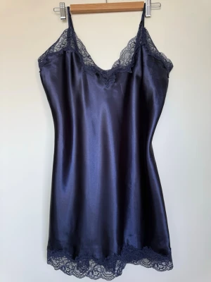 Mörkblått nattlinne från Boux Avenue - Snyggt mörkblått nattlinne  från Boux Avenue med spetsdetaljer vid halsringning och nederkant. Tunna axelband och figurnära passform ger en elegant look. Perfekt för mysiga kvällar hemma.