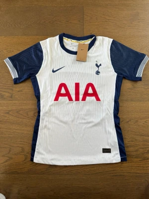 Tottenham Hotspur matchtröja Nike - Vit och marinblå Tottenham Hotspur matchtröja från Nike med AIA-logga på bröstet och spelarnamn 'VAN DE VEN' samt nummer 37 på ryggen. Korta ärmar, klubbmärke på bröstet och tillverkad i lätt funktionsmaterial.