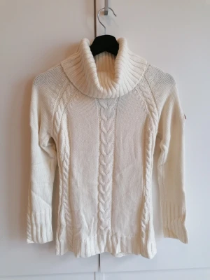 Stickad polotröja i kashmirblandning - Snygg vit stickad polotröja med bred krage och klassiskt flätmönster. Tröjan har långa ärmar, ribbade muddar och en brun patch på ena ärmen. Perfekt för kalla dagar och enkel att matcha. Gjord i en lyxig mjuk viskos-, ull- och kashmirblandning. 