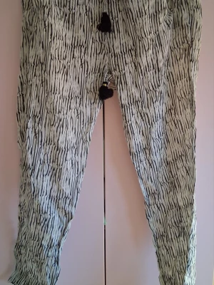 Mönstrade linnebyxor med snörning - Säljer ett par vita linnebyxor med svart abstrakt mönster och snörning i midjan med tofsar. Byxorna har avslappnad passform och är perfekta för en chill och trendig look. Materialet känns lätt och luftigt, perfekt för varma dagar.