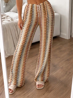 Mjukisbyxor med retro mönster - Säljer ett par mjukisbyxor med snyggt retroinspirerat mönster i brunt, beige, blått och vitt. Byxorna har utsvängda ben, dragsko i midjan och är gjorda i ett mjukt, stretchigt material. Perfekta för en chill och trendig look.