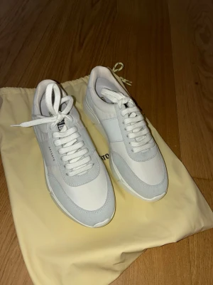 Vita sneakers från Axel Arigato - Snygga vita sneakers från Axel Arigato med stilren design. Skorna har ovandel i läder och mocka, vita skosnören och en chunky sula. Märkeslogga på sidan och plös. Perfekta för dig som gillar minimalistisk och modern stil.