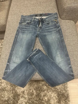 Blå jeans från Replay - Snygga blå jeans från Replay med klassisk femficksdesign och slitningar på både fram- och baksidan. Jeansen har raka ben och detaljer som kontrastsömmar och läderpatch bak i midjan. Perfekta för dig som gillar en avslappnad och trendig look.