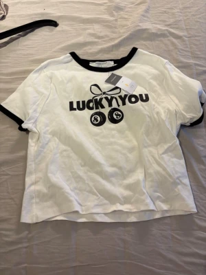 Vit t-shirt med svart tryck från Primark - Vit T-shirt med svart tryck från primark. Den är svart vid armarna och halsen. Helt splitterny, den är aldrig använd