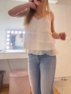 Vit volangig linnetopp från VeroModa - Säljer en söt vit linnetopp från VeroModa med tunna axelband och v-ringning. Toppen har flera lager volanger i ett lätt och luftigt material, perfekt för varma dagar. Enkel att styla med jeans eller kjol för en fräsch look.