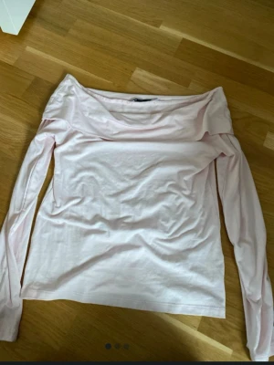 Ljusrosa offshoulder topp - Snygg ljusrosa offshoulder topp med långa ärmar. Toppen har en bred krage som vilar över axlarna och är tillverkad i mjukt bomullsmaterial. Perfekt för dig som gillar en stilren och feminin look.