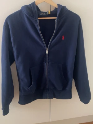 Mörkblå hoodie från Polo Ralph Lauren - Mörkblå hoodie med dragkedja från Polo Ralph Lauren. Denna säljer jag av att jag inte använder den alls. Kan vara perfekt att bara ha med på en sommarkväll.