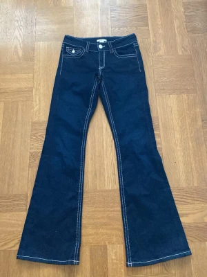 Mörkblå bootcut jeans med kontrastsömmar - Snygga mörkblå bootcut jeans med vita kontrastsömmar och klassiska fem fickor. Jeansen har utsvängda ben, low rise och detaljerade bakfickor med knappar. Perfekta för en trendig och avslappnad stil. Säljer dem för att de inte passar. Aldrig använda❤️Orginalpris 400 skriv om du har några frågor. Priset kan enkelt förhandlas