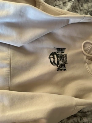 Beige hoodie från YOURTURN - Snygg beige hoodie från YOURTURN med svart grafiskt tryck på bröstet. Hoodien har dragsko i huvan och är tillverkad i mjukt material som känns skönt mot huden. Perfekt för en avslappnad och trendig look.