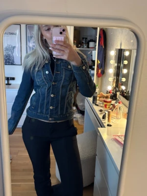 Klassisk blå jeansjacka - Snygg blå jeansjacka med figurnära passform och silverfärgade knappar framtill. Jackan har två bröstfickor med lock och sömdetaljer som ger en cool look. Perfekt att slänga över en t-shirt eller hoodie för en avslappnad stil.