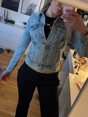 Ljusblå jeansjacka med klassisk passform - Säljer en snygg ljusblå jeansjacka med klassisk krage och knappstängning framtill. Jackan har två bröstfickor med lock och sömmar som ger en schysst siluett. Perfekt att slänga över en t-shirt eller hoodie för en cool look.