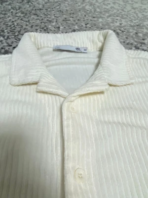 Vit ribbad skjorta med kort ärm - Säljer en vit skjorta från 157 med korta ärmar och ribbad struktur. Skjortan har klassisk krage och knappar framtill, perfekt för dig som gillar en clean och enkel look. Materialet känns mjukt och bekvämt mot huden.