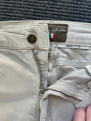 Beiga jeans från Cavaliere - Snygga jeans från Cavaliere med klassisk rak passform och dragkedjegylf. Tillverkade i mjukt bomullstyg med diskreta detaljer och italiensk flagga på insidan av linningen. Perfekta för en stilren och avslappnad look.