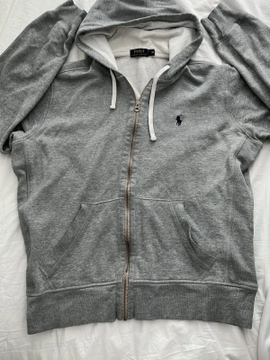 Grå zip hoodie från Polo Ralph Lauren - Snygg grå hoodie med dragkedja från Polo Ralph Lauren. Klassisk design med huva och vita snören, två fickor fram och mörkblå broderad logga på bröstet. Tillverkad i mjuk bomullsblandning som är skön att ha på sig. Hör av dig vid frågor o priset kan självklart diskuteras😄