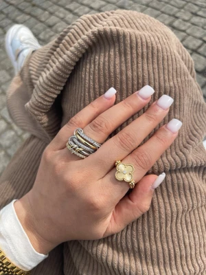 Blå och gul klöverring två sidigt guldpläterad, hypoallergenic  - Säljer en unik ring med klöverformad detalj i blått och guld. Ringen har en elegant pärlstruktur runt klövern och bandet, vilket ger en lyxig känsla. Perfekt för dig som vill sticka ut med accessoarer som har både färg och form.  Har storlek 7 och 8