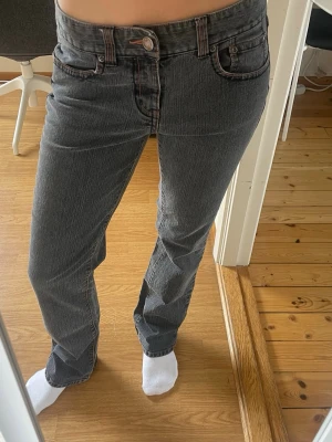 Grå raka jeans med kontrastsömmar - Säljer ett par grå jeans med raka ben och snygga kontrastsömmar, inklusive en unik broderad detalj på bakfickan. Klassisk femficksmodell och normalhög midja. Perfekta för en avslappnad och trendig look.