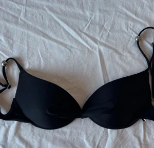 Svart bikini med pärldetaljer - Svart bikini med dekorativa pärldetaljer på axelbanden. Kuporna är lätt vadderade. Justerbara axelband. Märket är Ellos (ena kupan är lite knottrig högst upp, se bild i annons)!🖤