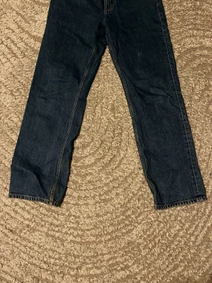 Mörkblå raka jeans från Levi's - Säljer ett par klassiska mörkblå jeans från GANT med raka ben och femficksmodell. Jeansen har tydliga kontrastsömmar och en läderpatch med logga bak i midjan. Perfekta för en avslappnad och tidlös stil.