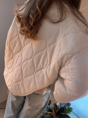 Vit quiltad cardiganjacka Gina Tricot - Snygg vit quiltad cardiganjacka med rund halsringning och fina knappar framtill. Jackan är tllverkad i ett mjukt, strukturerat tyg. Perfekt för våren och sommaren som jacka eller som kofta för att styla snyggare outfits🌷Jag brukar ha S/M men har L i denna jacka för att den var liten i storleken. Hör gärna av dig vid frågor.