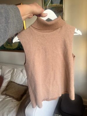 Beige ärmlös polotröja från Zara - Stickad ärmlös polotröja från Zara i en mjuk beige nyans. Tröjan har en hög ribbad polokrage och rak passform.