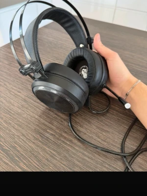 Svarta gaminghörlurar med kabel - Säljer ett par svarta over-ear gaminghörlurar från MSI med kabelanslutning. Hörlurarna har vadderade kåpor och justerbart huvudband i konstläder och plast. Perfekta för gaming med snygg design och bekväm passform.