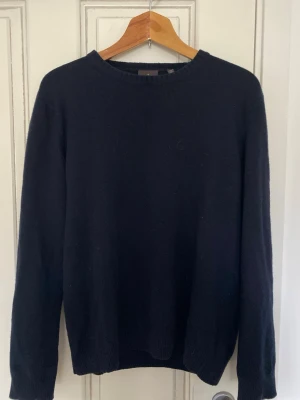 Mörkblå Kashmir tröja från Oscar Jacobsson  - En enkel och stilren mörkblå stickad kashmir tröja med rund halsringning och långa ärmar. Tröjan har ribbade muddar vid ärmslut och nederkant. Perfekt basplagg till garderoben och passar till det mesta.