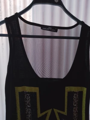 Svart linnetopp Philipp Plein - Cool svart linnetopp från Philipp Plein med stora blixtar i leopardmönster och gula detaljer framtill. Tryck med årtalet 1978 och märkets namn. Perfekt för dig som gillar statement-plagg och djurmönster.