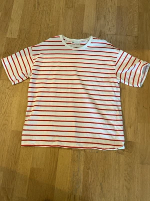 Vit och röd randig t-shirt Pull&Bear - Säljer en vit t-shirt från Pull&Bear med röda horisontella ränder. Klassisk rund halsringning och korta ärmar. Materialet är väldigt skönt på huden. Tröjan passar för både män och kvinnor. Perfekt nu för sommaren.