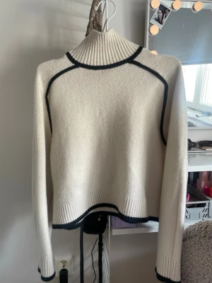 Vit stickad tröja med svarta detaljer H&M - Säljer en vit stickad tröja från H&M med svarta kontrastdetaljer längs sömmarna och kanterna. Tröjan har hög ribbad. Materialet är mjukt och bekvämt. Mycket fin till en clean outfit❣️