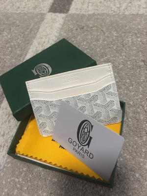 Goy4ard plånbok vit - Snyggt och stilrent kortfodral från Goy4ard i grått med klassiskt mönster och logotyp. Fodralet är tillverkat i läder och har flera fack för kort. Kommer med original ask och tygpåse. Perfekt för dig som vill ha något exklusivt och trendigt.