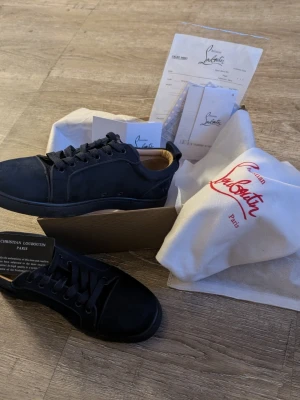 Mörkblå sneakers från Christian Louboutin - Stilrena svarta sneakers från Christian Louboutin i mocka med klassisk låg siluett. Skorna har svarta skosnören, diskreta sömmar och en svart yttersula. Kommer med originalkartong, dustbag och äkthetskort.
