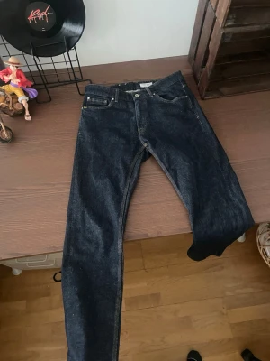 Mörkblå jeans från Tiger of Sweden - Säljer ett par mörkblå jeans från Tiger of Sweden, modell 903. Klassisk femficksdesign med raka ben och snygga kontrastsömmar. Jeansen är tillverkade i slitstark denim och har en tidlös look som passar till det mesta. Aldrig använt 