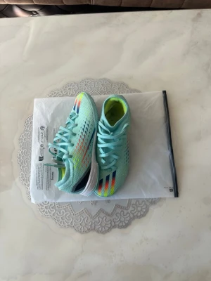 Adidas fotbollsskor inomhus - Säljer ett par snygga turkosa Adidas fotbollsskor med färgglada detaljer i rött, gult och blått på ovandelen. Skorna har snörning, låg profil och ovandel i meshmaterial för bra ventilation. Perfekta för dig som vill sticka ut på planen!