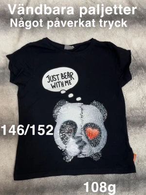 Svart t-shirt med panda och paljetter - Cool svart t-shirt med vändbara paljetter som formar ett pandaansikte och ett rött hjärta. Trycket har texten 'Just bear with me' i en pratbubbla. Perfekt för dig som gillar unika detaljer och lekfull design.🌸 Fint använt skick. Vändbara paljetter. Något slitet tryck. Storlek 146/152 