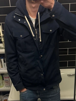 J.Lindeberg-Blå-Fieldjacka - Snygg mörkblå vindjacka från J.Lindeberg med dragkedja och tryckknappar framtill. Jackan har två bröstfickor med lock och knappar samt två sidofickor. Klassisk rak passform och diskret logga på ärmen. Använd men fortfarande i fint skick. Storlek S men passa bra för M också.        Skriv vid fler frågor eller funderingar.