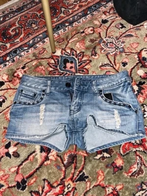 Blå jeansshorts med slitningar - Midjemått: 37cm🥰 Snygga blå jeansshorts med slitna detaljer framtill och klassiska fem fickor. Shortsen har låg midja och råa kanter för en cool look. Perfekta för sommaren och enkla att matcha med olika toppar. 
