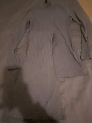 Ljusgrått ribbat set med långärmad topp - Säljer ett ljusgrått ribbat set med långärmad topp och matchande byxa. Setet har en enkel och stilren design med smal ribbstruktur och mjukt material som känns skönt mot huden. Perfekt för dig som gillar en clean och bekväm look.