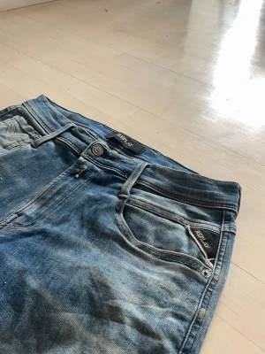 Replay Anbass - Snygga blå jeans från Replay med klassisk femficksdesign och slitningar för en cool look. Jeansen har en normal midja och raka ben, tillverkade i denim med tydliga detaljer och logotyp på fickan. Perfekta för dig som gillar en avslappnad stil.