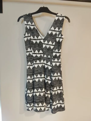 Svartvit ärmlös klänning med mönster - Cool svartvit klänning med v-ringad hals och ärmlös design. Klänningen har ett grafiskt mönster med trianglar och linjer som ger en modern look. Perfekt för dig som gillar att sticka ut och vill ha något unikt i garderoben. Nyskick 