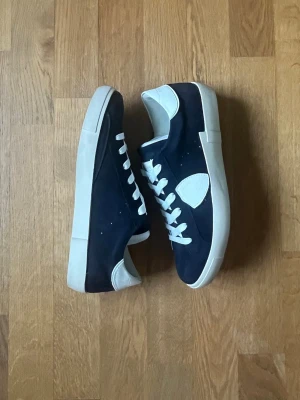  sneakers från Philippe Model - Snygga mörkblåa sneakers från Philippe Model med vita detaljer och vit sula. Skorna har vita skosnören, vit hälkappa och en vit logopatch på sidan. Materialet är en mix av mocka och läder, vilket ger en exklusiv känsla. Mycket bra skick
