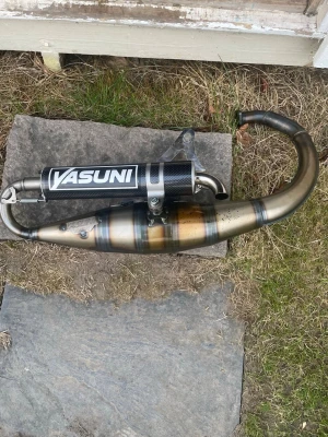 Yasuni avgassystem till moped - Säljer ett Yasuni avgassystem till moped. Utrustad med svart ljuddämpare i kolfiber-look och metallrör med snygga svetsningar och blå-bruna nyanser. Passar dig som vill ha bättre prestanda och coolare look på din moppen