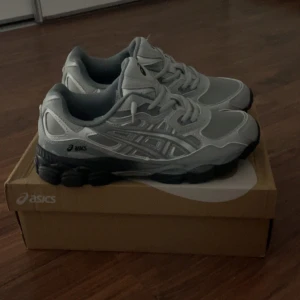 Gråa Asics sneakers med svart sula ( Pris kan diskuteras) - Snygga sneakers från Asics i olika nyanser av grått med detaljer i mesh och syntet. Skorna har en chunky svart sula och klassisk snörning. Perfekta för dig som gillar sportig och stilren look.