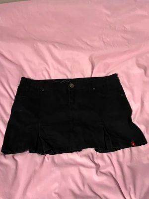 Edc by Esprit Svart Kjol - Stilren svart kjol från edc by Esprit i en trendig Y2K-inspirerad modell. Kjolen har en lågmidjad passform och en lätt utsvängd design som ger en feminin siluett. Perfekt att styla med toppar, hoodies eller crop tops för en modern streetwear-look eller mer uppklätt.